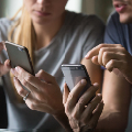 Two people hold smartphones, sitting closely, concentrating on screens, in a well-lit indoor setting.